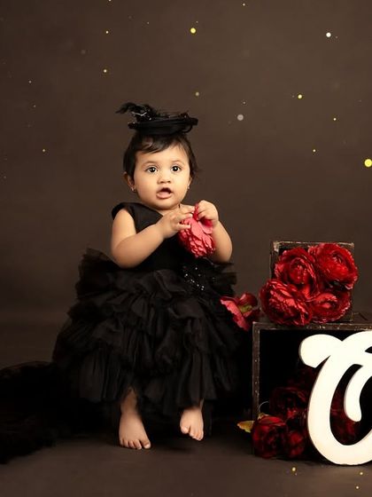 A sweet, seated portrait with a 'One' sign and a box of red roses. The dark background makes the subject and props stand out beautifully.