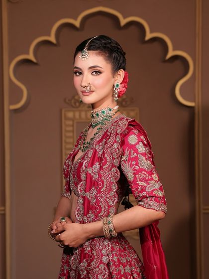 This bride's look is the epitome of grace. Her makeup is soft and radiant, with a natural lip color that complements the deep red of her embroidered lehenga and the fresh flower in her hair.