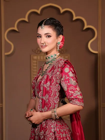 This bride's look is the epitome of grace. Her makeup is soft and radiant, with a natural lip color that complements the deep red of her embroidered lehenga and the fresh flower in her hair.