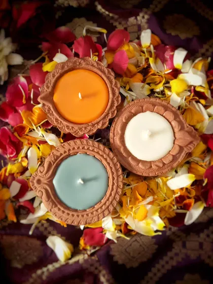 An overhead shot of the unlit tri-color Diya Candles, nestled in a bed of colorful flower petals. The saffron, white, and green wax represents a beautiful tribute to our nation's spirit.