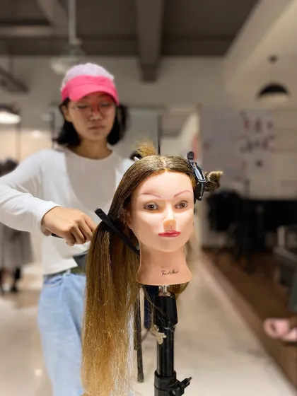 A student fully concentrated on her hairstyling practice. Our program provides ample time for students to hone their craft.