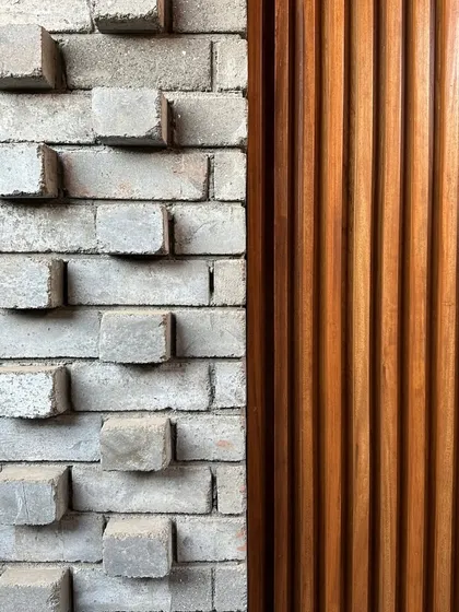 A close-up of materials in progress. The contrast between the textured, protruding brickwork and the smooth, vertical wooden slats is a study in material honesty.