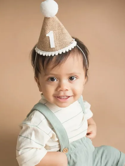 A sweet close-up of a one-year-old boy in his party hat. The soft, neutral background ensures that his adorable face and happy expression are the stars of the show.