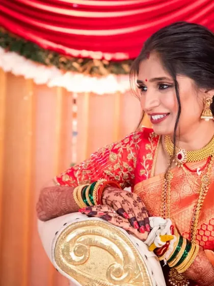 A beautiful candid shot of the bride during her wedding events. The soft, side-swept hairstyle is adorned with a floral arrangement, adding a touch of freshness to her traditional orange saree.