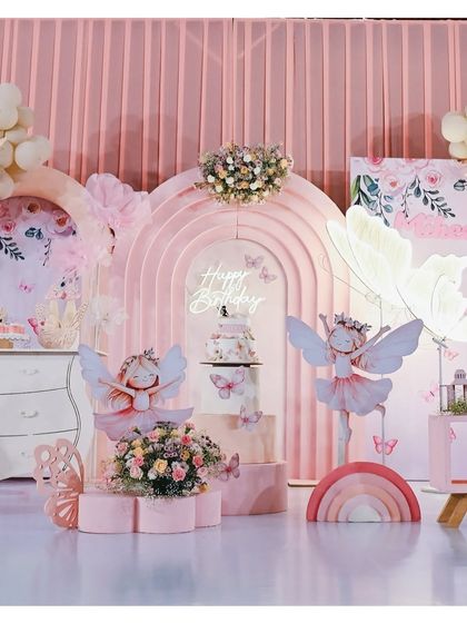 A full view of the pink fairy and butterfly themed stage. It features two large fairy cutouts, a butterfly-shaped cake stand, and a backdrop of layered pink arches, creating a dreamy and cohesive look.