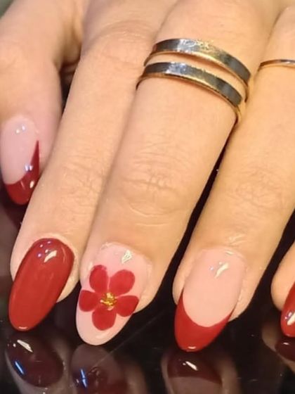 A beautiful red manicure with a floral accent nail and modern, abstract red tips.