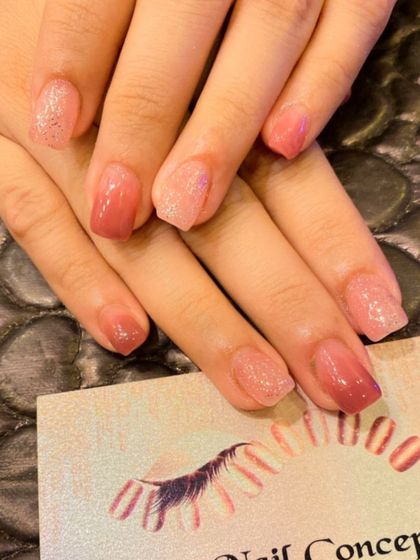 A subtle and shimmery set of short, square nails. The design features a mix of sheer pink and glittery pink polishes for a soft, multi-tonal look.