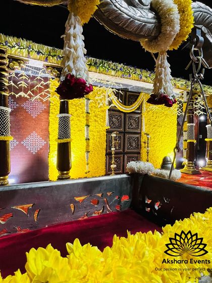 A close-up of a naming ceremony cradle, set against a magnificent backdrop of yellow flowers and ornate temple-style pillars. The warm lighting enhances the golden hues of the decor.