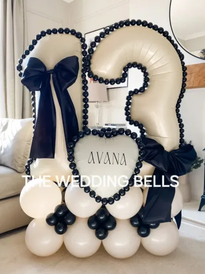A chic and modern balloon bouquet for a 13th birthday. The black and white color scheme with large satin bows gives it a sophisticated look, and the personalized 'Avana' heart balloon makes it a unique centerpiece for the celebration.