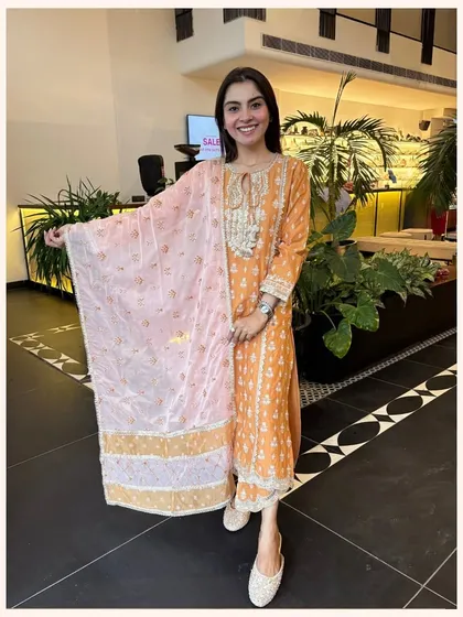 This orange kurta set features a contrasting pink dupatta for a fun and colorful look. The intricate neckline embroidery adds a touch of festive charm.