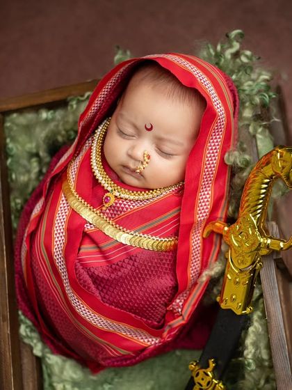 An overhead view of the Rajmata Jijabai setup, showing the baby nestled in a rustic wooden crate with a soft green lining, creating a beautiful color contrast with the red saree.