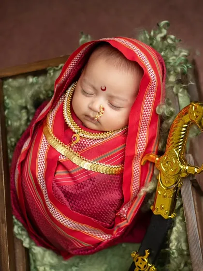 An overhead view of the Rajmata Jijabai setup, showing the baby nestled in a rustic wooden crate with a soft green lining, creating a beautiful color contrast with the red saree.