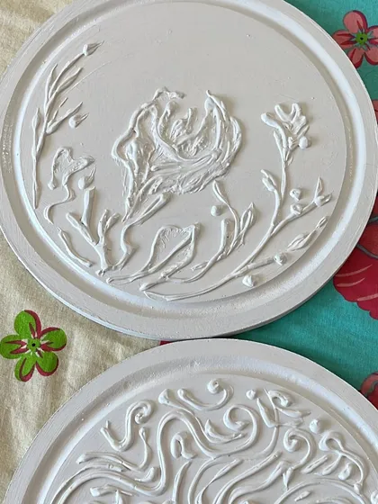 Both of the circular textured plaques together. One has a floral, organic design, while the other is more of a geometric swirl, creating a beautiful pairing.