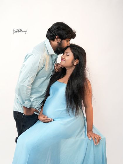 A tender moment between a couple, with the husband-to-be kissing his wife's forehead. The soft blue gown and simple background keep the focus on their love and connection.