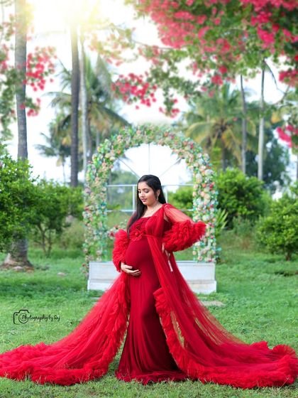 A stunning outdoor portrait in a vibrant red ruffled gown. The lush greenery and floral arch create a perfect backdrop for this glamorous maternity shoot.