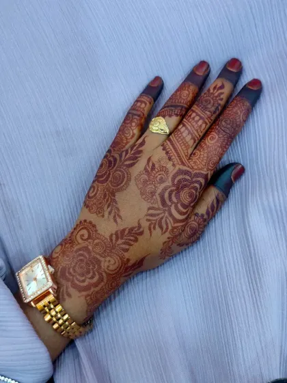 This photo highlights the rich, dark stain of a floral henna design on the back of the hand, complete with filled-in fingertips.
