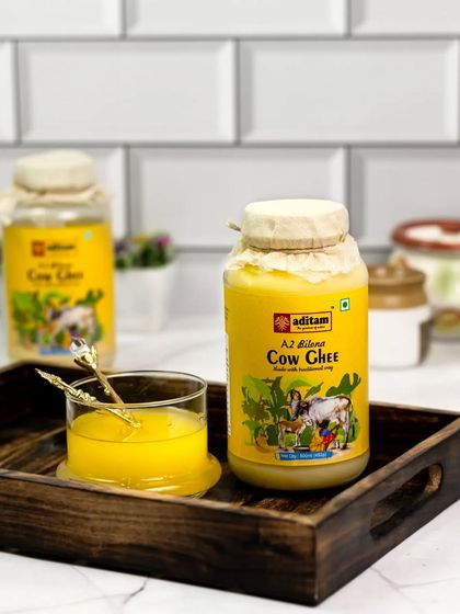 This is one of my favorite shots. A jar of pure cow ghee is presented on a rustic wooden tray with a glass of liquid ghee, creating a clean, bright, and appealing image against a white tiled background.