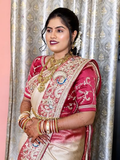 Another angle of the beautiful bride in her cream and red saree, showing her radiant smile and the flawless finish of her makeup.