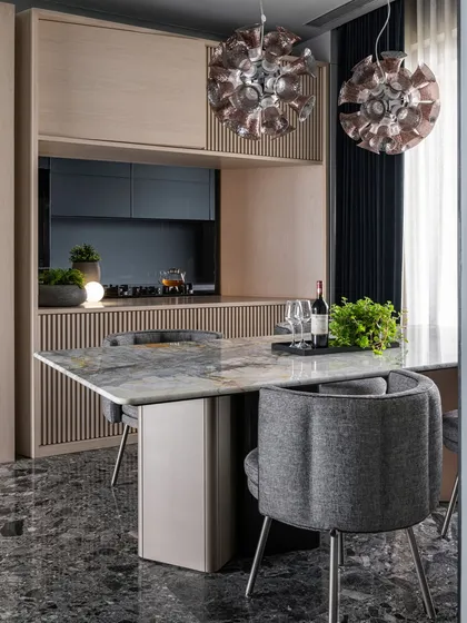 The dining area in our 'Wedged Haus' project is defined by the monolithic presence of the kitchen block. We used light oak veneer and ribbed details to create a standalone object that contrasts with the muted grey tones and Ceppo De Gre marble flooring. Statement pendant lights from Moooi anchor the space, making the dining experience both intimate and visually striking.