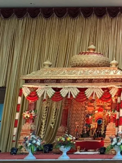 A glimpse of a grand, temple-inspired wedding mantap. The golden structure, intricate carvings, and traditional red and white floral decorations replicate the sanctity and grandeur of a temple wedding.