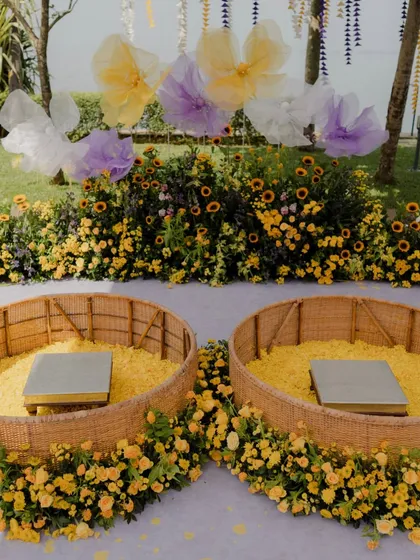 The twin seating arrangement for the couple at the pastel Haldi ceremony. The wicker baskets are filled with marigold petals and surrounded by a bed of sunflowers and other yellow blooms.