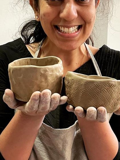 The proud creator holding up two hand-built bowls, each with a unique, rustic texture.