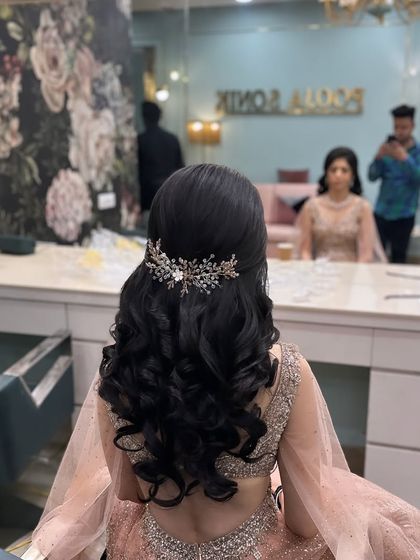 A classic engagement hairstyle with a half-up twist, tight curls, and a sparkling leaf-design accessory. This look is created in a salon setting.