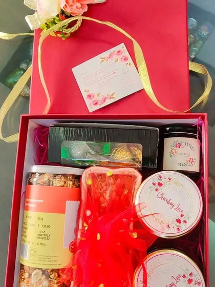 Inside the red gift box: a curated selection of treats including a dry fruit cake, jars of snacks, and a box of chocolates.