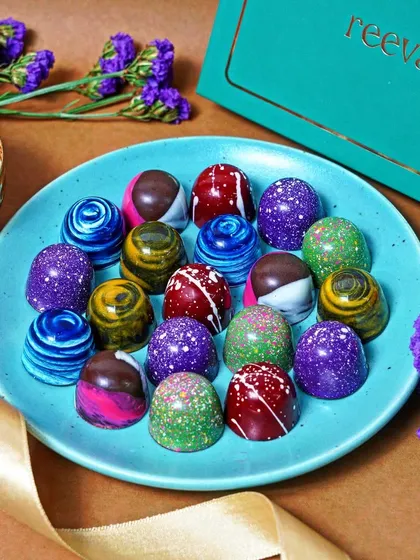 A flat lay of colorful, handcrafted bonbons on a blue plate, styled with flowers and ribbon. This overhead shot emphasizes the artistry and premium quality of the chocolates, ideal for product catalogs.