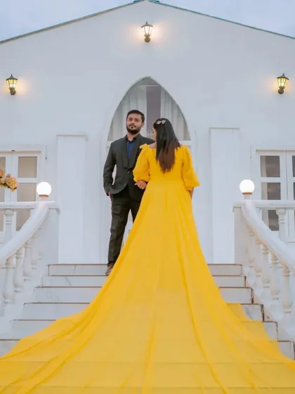 A dramatic shot from behind, showcasing the incredible length and color of the bride's yellow trail gown. This angle emphasizes the grandeur of the outfit and the unique location.
