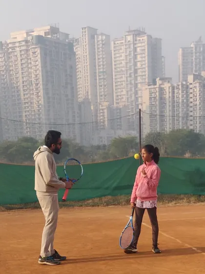 A moment of instruction on the court. Our coach discusses technique with a junior player against the backdrop of our urban training facility, highlighting our focus on personalized feedback.