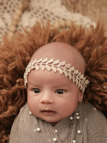 A beautiful close-up of a newborn baby girl, awake and looking at the camera. Her delicate headband and the soft, furry rug create a sweet and gentle portrait.