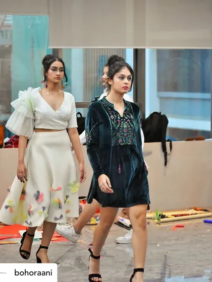 Our designs on the runway for the Bohoraani showcase. This photo captures a model wearing our white ruffled blouse and floral appliqué skirt, alongside another model in a dark green velvet tunic dress with detailed embroidery.