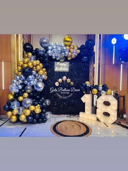 A cool and sophisticated 18th birthday party setup with a black backdrop, a gold and silver balloon arch, and disco balls.