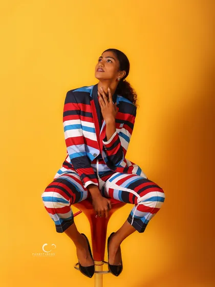 A striking pose against a solid yellow background. The bold, colorful suit and thoughtful expression create a piece of wearable art.