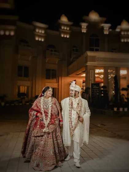 A classic portrait of the couple taking a stroll outside their grand wedding venue at night. The architectural beauty and the warm lighting add a touch of royalty to their first walk as husband and wife.