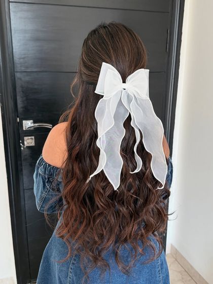 A soft, half-up hairstyle with long, flowing waves, finished with a pretty white organza bow. This is a very romantic and feminine look.
