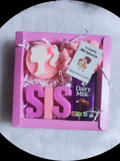 A sweet Rakhi gift for a sister. This pink hamper includes "SIS" letter soaps, a Barbie soap, a scrunchie, and a Dairy Milk chocolate.