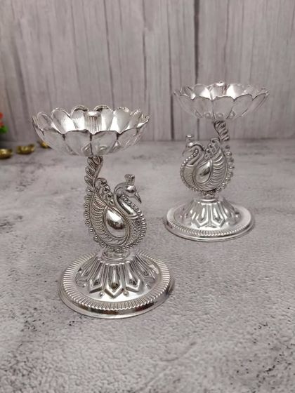 A pair of newly designed peacock diyas in German silver. The lotus-shaped bowl sits atop a beautifully crafted peacock base, blending elegance and tradition.