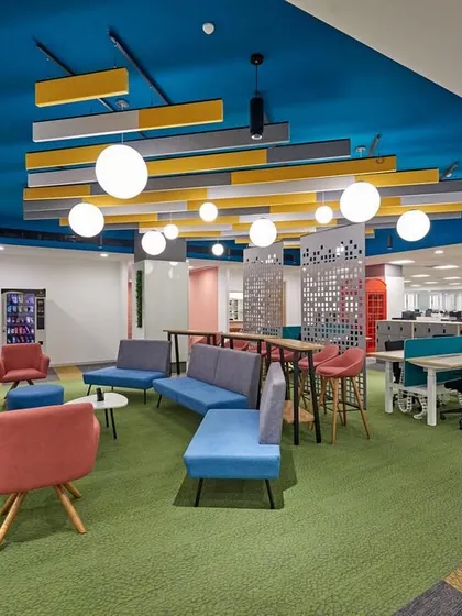 A vibrant collaboration area with a bright blue ceiling and a custom light fixture. The space is furnished with colorful, modern sofas and chairs on a green carpet.