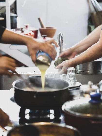 A student adds liquid to a pot, a crucial step in building a sauce. Our program covers the science behind cooking, from emulsions to reductions.