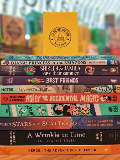 A stack of our favorite graphic novels for young readers, including 'Aster and the Accidental Magic' and 'Diana: Princess of the Amazons'.