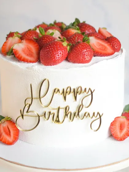 A classic Red Velvet cake with a modern twist. The cake is filled with fresh strawberries and cream cheese frosting, and the outside is finished with a simple white velvet texture and a "Happy Birthday" topper.