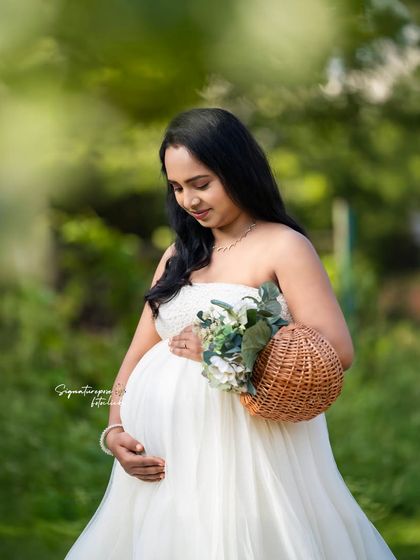 A quiet, intimate moment captured outdoors. The focus is on the mother cradling her bump amidst soft greenery.