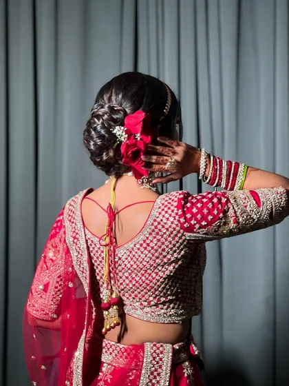 A back view of the bride's hairstyle, featuring a classic bun adorned with red roses and a delicate hair accessory.