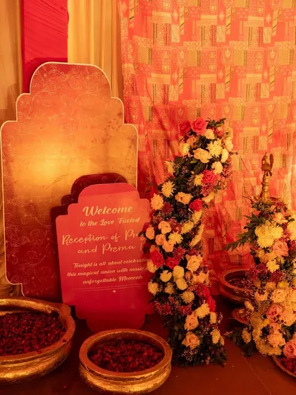 A multi-panel, layered welcome sign in shades of red and gold, placed amidst bowls of rose petals for a luxurious reception entrance.