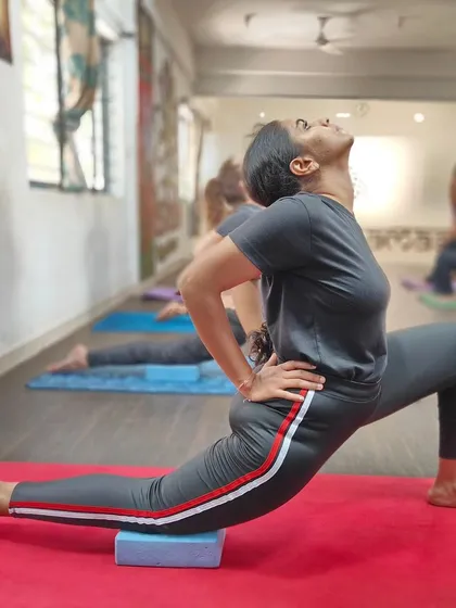A student uses a block under her knee in a low lunge (Anjaneyasana) to ensure proper alignment and support.