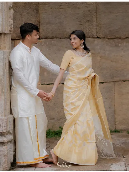 A couple holds hands by a stone wall, their traditional attire and gentle interaction creating a classic portrait.