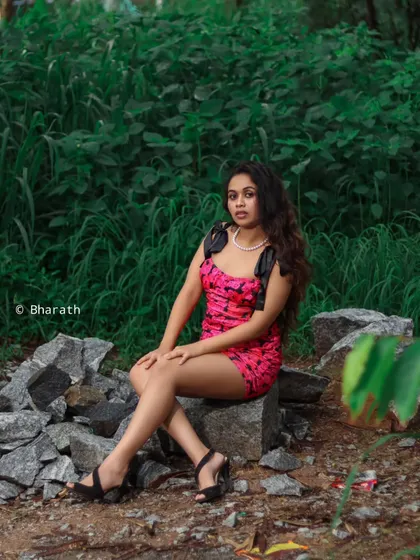 A wider shot of the model seated on rocks. The composition balances the bright dress with the natural, earthy tones of the location.