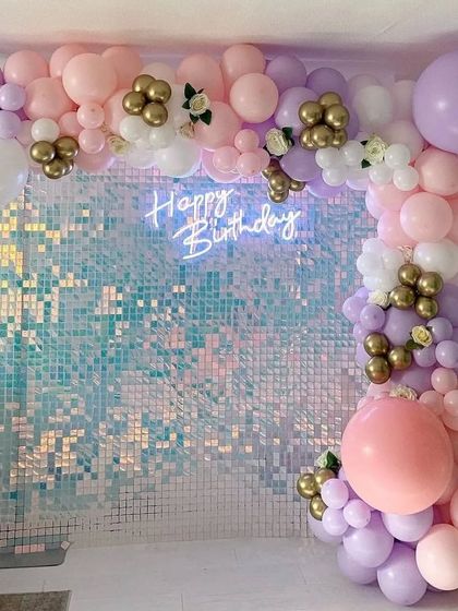 A dreamy pastel decoration with a sequin wall and a balloon arch in lavender, pink, and gold.